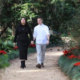 Engaged couple walking along a garden pathway surrounded by blooming flowers at Washington Oaks Gardens, Palm Coast, Florida.