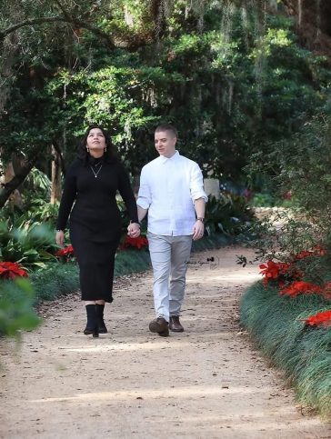 Engaged couple walking along a garden pathway surrounded by blooming flowers at Washington Oaks Gardens, Palm Coast, Florida.