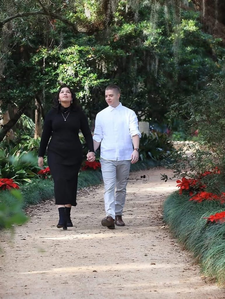 Engaged couple walking along a garden pathway surrounded by blooming flowers at Washington Oaks Gardens, Palm Coast, Florida.