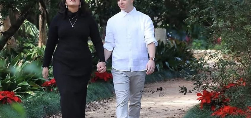 Engaged couple walking along a garden pathway surrounded by blooming flowers at Washington Oaks Gardens, Palm Coast, Florida.